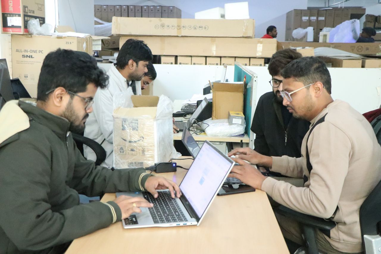 Team members working on laptops among boxed SNL All-in-One PCs