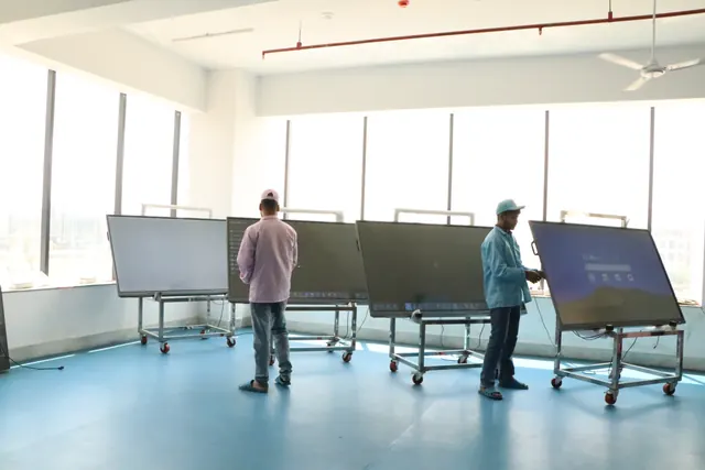 Two technicians checking large interactive panels on wheeled stands in a bright factory hall